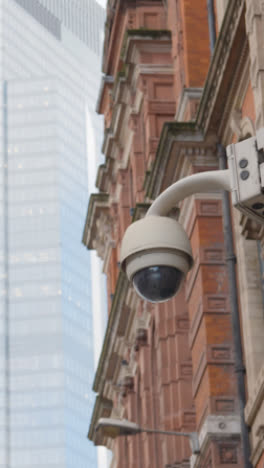 Vertical-Video-Close-Up-Of-Surveillance-Camera-Outside-Modern-Office-Buildings-In-City-Of-London-UK